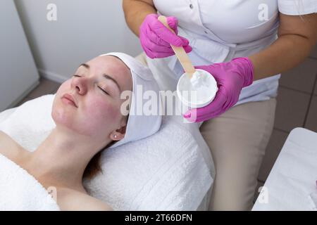 Cropped Cosmetologist, Beautician Applied Moisturizing Mask, Creme on Women's Red skin After Chemical Peeling in Beauty Salon. Kosmetologie Und Gesicht Stockfoto