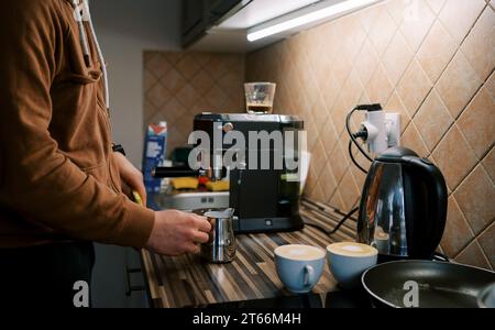 Der Barkeeper klopft das Milchkännchen auf den Tisch, um den Schaum nach dem Aufschäumen der Milch zu setzen Stockfoto