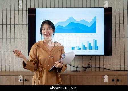 Eine selbstbewusste und professionelle asiatische Geschäftsfrau oder Finanzanalytikerin stellt ihre Informationen zur Finanzanalyse in der Besprechung vor. Stockfoto