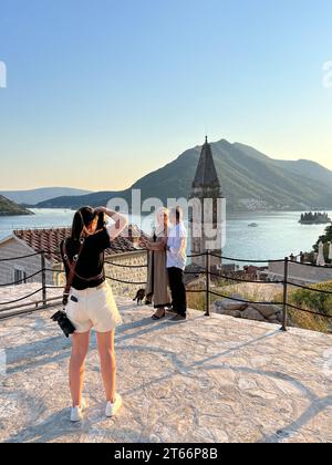 Perast, Montenegro - 03. august 2023: Fotografin fotografiert Mann und Frau auf einer Aussichtsplattform in der Nähe der Nikolaikirche. Perast, Montenegro Stockfoto