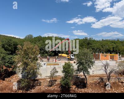 Budva, Montenegro - 05. august 2023: Betonpumpe gießt das Fundament auf einer Baustelle zwischen grünen Bäumen Stockfoto