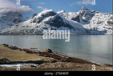 Genießen Sie den wunderschönen Stortind Berggipfel und die Seen der Flakstadpollen Bucht, Flakstadøy, Lofoten, Norwegen Natur, Winterschnee gegen blauen Himmel, Turquo Stockfoto