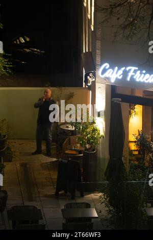 Ein kahler Mann raucht, während er an einem Winterabend beiläufig vor einem Café steht, Wien Österreich, Stockfoto