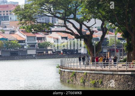 Eine weibliche Reiseleiterin mit Führerschein führt natürlich eine Gruppe von Besuchern entlang des Flusses Singapur, um die Wahrzeichen und malerischen Orte der Stadt zu erkunden. Stockfoto