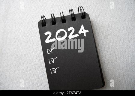 Neujahrsvorsätze 2024 über schwarzes Spiralheft. 2024 Zielliste mit Notizbuch. Lösungen, Plan, Ziele, Maßnahmen, Checkliste, Ideenkonzept. Neujahr Stockfoto