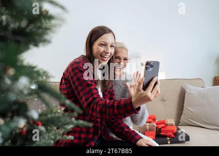 Feiern Sie Weihnachten, Silvester, Mutter und Tochter halten ein Smartphone-Selfie und machen Sie Fotos, grüßen Sie während der sozialen Distanz per Videoanruf Stockfoto