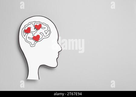 Emotionales Denken. Papierausschnitt des menschlichen Kopfes mit Zeichnung des Gehirns und der roten Herzen auf grauem Hintergrund, Draufsicht. Leerzeichen für Text Stockfoto