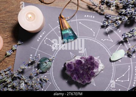 Astrologie-Vorhersage. Zodiakrad, Edelsteine, brennende Kerze und Lavendel auf Holztisch, flache Ladefläche Stockfoto