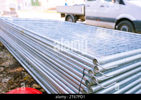 Stapel von verzinkten Teilen für temporäre Metalldrahtzaunplatten werden auf der Straße gestapelt und können auf der Baustelle montiert werden. Stockfoto