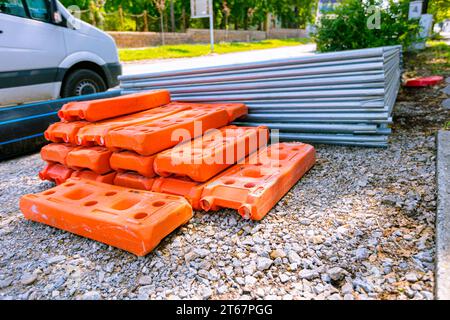 Stapel, Haufen von verzinkten Teilen für temporäre Metallzaunplatten werden gestapelt und ein hohler Kunststoffzaunfuß auf der Straße, bereit für die Montage am Bau Stockfoto