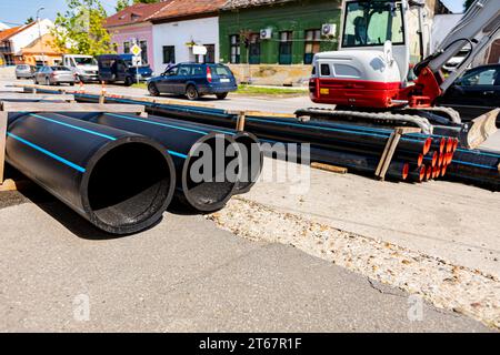 Nur wenige neue Kunststoff-Wasserleitungen sind auf der Straße gestapelt und können auf der Baustelle in den Graben verlegt werden. Stockfoto