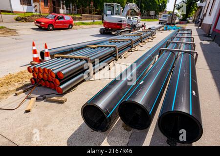 Nur wenige neue Kunststoff-Wasserleitungen sind auf der Straße gestapelt und können auf der Baustelle in den Graben verlegt werden. Stockfoto