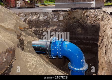 Kupplung mit Schrauben zur Verbindung von großen Rohrleitungen, Kunststoffrohr mit Metallbogen der unterirdischen Wasserversorgung. Unvollendetes Projekt, unverschütteter Graben Stockfoto