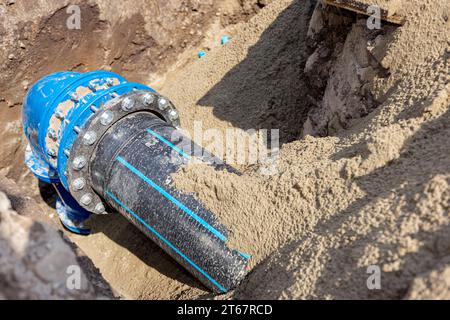 Kupplung mit Schrauben zur Verbindung von großen Rohrleitungen, Kunststoffrohr mit Metallbogen der unterirdischen Wasserversorgung. Unvollendetes Projekt, unverschütteter Graben Stockfoto