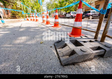 Barrikade vor der Baustelle neben der Stadtstraße mit aktivem Verkehr installiert. Mobiler Metallzaun mit Kunststofffuß sorgt für Stabilität der Tempora Stockfoto