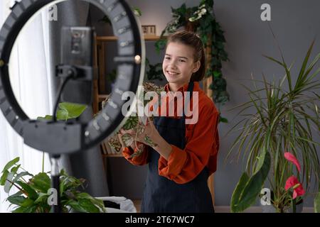 Video-Blog über Zimmerpflanzen. Das Kind, das im Frühjahr den Fluss über die Pflege der Zimmerpflanze führt, verwendet ein Smartphone und eine Ringlampe Stockfoto