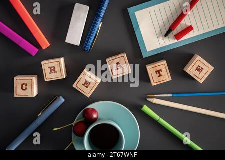Flache Anordnung eines kreativen Schreibtischs mit „CREATE“ in Holzblöcken, umgeben von Bastelbedarf und einer Tasse Kaffee. Stockfoto