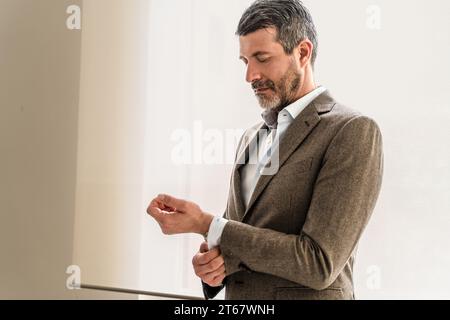 Ein reifer Geschäftsmann passt seine Hemdmanschette sorgfältig an und betont die Aufmerksamkeit auf das professionelle Erscheinungsbild. Stockfoto