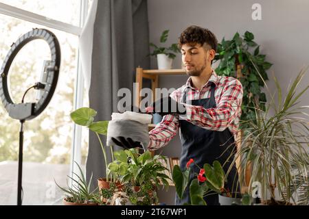 Arabische männliche Gärtner Influencer Filme Video für Blog gibt Empfehlungen, wie man Topfblume transplantiert Stockfoto