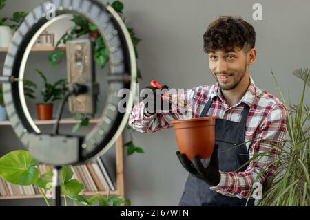 Arabische männliche Gärtner Influencer Filme Video für Blog gibt Empfehlungen, wie man Topfblume transplantiert, Gießen Drainage sendet Livestream Stockfoto