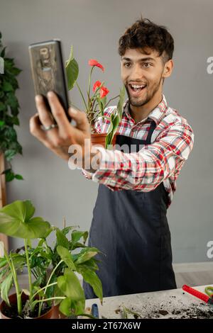 Foto eines arabischen Gärtners, der über Blumen steht, Pflanzen im Gewächshaus machen Selfie per Handy. Stockfoto