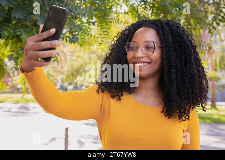 Afroamerikanerin lächelt und macht draußen ein Foto von sich mit einem Smartphone. Stockfoto