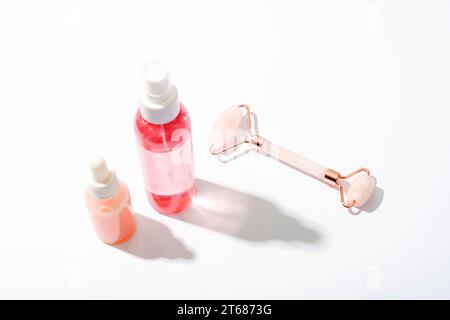 Rosa Kosmetikflaschen und rosa Quarzkristall Gesichtsrolle auf weißem Hintergrund mit starken Schatten. Naturkosmetik, Hautpflegekonzept. Draufsicht. Stockfoto