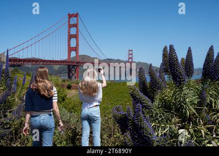 San Francisco, Kalifornien - 23. April 2023: Rückansicht der weiblichen Touristen, die die Golden Gate Bridge fotografieren, während sie mit einem Freund während des sonnigen Tages stehen Stockfoto