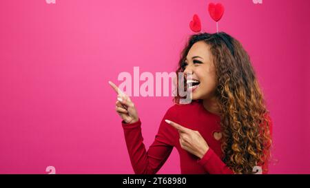 Lächelnde junge Frauen zeigen mit zwei Fingern auf Kopierraum, Valentinstag-Promotion Stockfoto