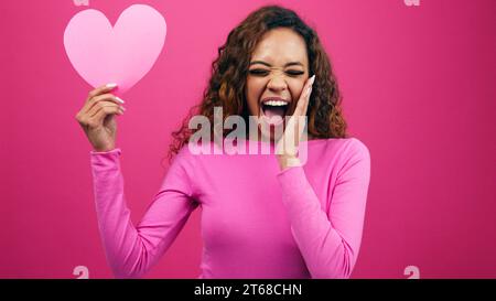 Überraschte junge Frau findet Liebe, schockiertes Gesicht, das Herz anschaut, Studio Stockfoto