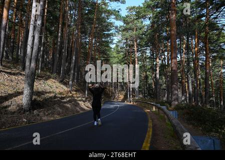 Ein junger erwachsener Radfahrer, der mit dem Fahrrad eine malerische, von Bäumen gesäumte Straße im Vordergrund der majestätischen Berggipfel hinunterfährt Stockfoto