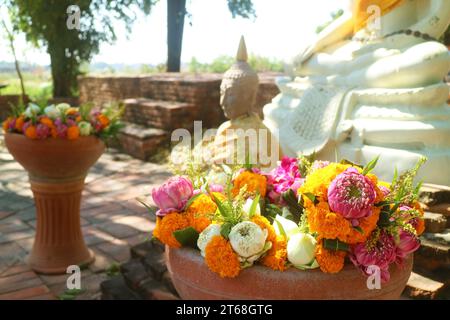 Bündel Lotus- und Ringelblumen für die Opfergabe in den Vasen mit unscharfen Buddha-Bildern im Hintergrund, Thailand Stockfoto