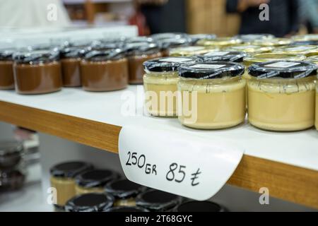 Gläser mit Creme auf dem Verkaufsregal mit Preisschild unter dem Glas auf schwarzem Hintergrund Stockfoto