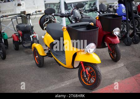 Moto-Elektrofahrzeuge sind in einer Reihe. Verleih von Elektrofahrrädern. Scheinwerfer an Fahrzeugen mit zwei Rädern. Motorradverkauf. Massenparkplätze für Fahrzeuge. Modern urban Stockfoto