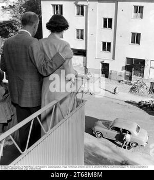 In den 1950er Jahren Ein Paar, das auf dem Balkon ihrer Wohnung auf die Straße unten blickt, wo ihr Auto geparkt ist und ein Kind auf einem Dreirad auf dem Bürgersteig fährt. Schweden 1955. Conard Stockfoto