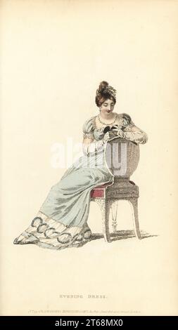 Regency Frau in vollem Abendkleid auf einem Stuhl sitzend, Blick auf ein Medaillon.. Himmlisch blaue Krabbenkittel über weißem Satin-Slip, tiefer Rand aus Netzspitze, Haare im griechischen Stil, Perlenkette. Vol. 13, Platte 4, 1. Januar 1815. Handkolorierter Kupferstich von Thomas Uwins aus Rudolph Ackermanns Repository of Arts, Strand, London. Stockfoto