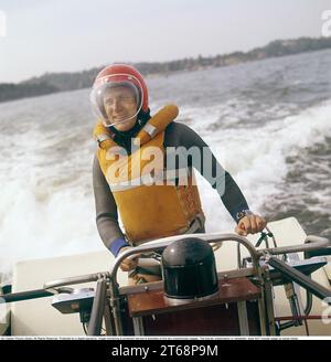 In den 1960er Jahren Ein Mann, der ein Motorboot fährt, gekleidet in einem Taucheranzug, einer Rettungsweste, einem Helm und einem Augenschutzglas. Er hat eine Hand am Lenkrad, eine am Gas. Schweden 1968. Kristoffersson Ref. DV13 Stockfoto