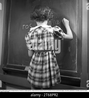 Schule in den 1940er Jahren Ein Mädchen vor dem Klassenzimmer an der Tafel, das mit einem Stück Kreide darauf schreibt. Schweden 1945 Kristoffersson Ref. P4-4 Stockfoto