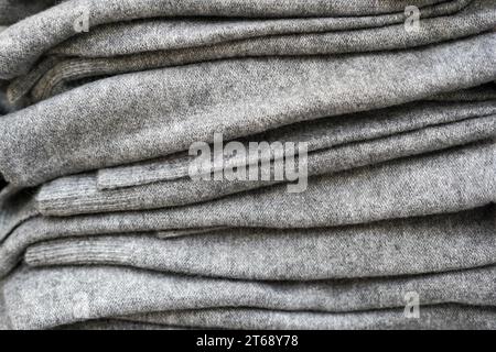 Stapel grauer gefalteter Strickpullover oder Pullover aus Wolle im Regal im Geschäft. Nahaufnahme mit warmer, bequemer, einfarbiger Kleidung für den Herbstsieg Stockfoto