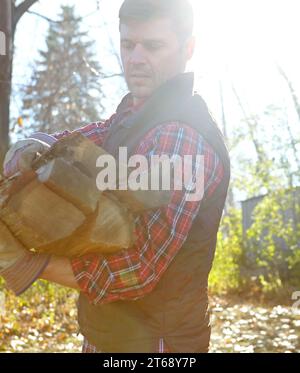 Ein reifer Holzfäller hält Holzstücke, nachdem er in abgelegener Landschaft einen Baum gehackt hat. Ernsthafter fokussierter Mann, der draußen allein steht und trägt Stockfoto