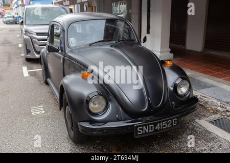 Ein schwarzes Chrom mit matter Farbe eines alten Volkswagen Käfers, der am Straßenrand geparkt ist. Orangefarbene Begrenzungsleuchten. Personenwagen. Singapur. Stockfoto