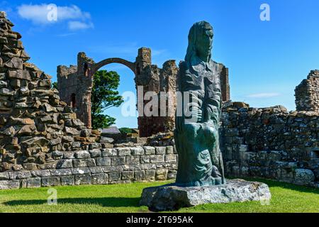 Statue von St. Cuthbert von Fenwick Lawson in der Lindisfarne Priory, Holy Island, Northumberland, England, Großbritannien. Der Rainbow Arch dahinter. Stockfoto