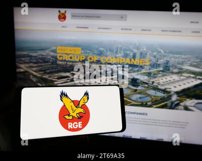 Person mit Smartphone und Logo der singapurischen Firma Royal Golden Eagle (RGE) vor der Website. Schwerpunkt auf dem Display des Telefons. Stockfoto