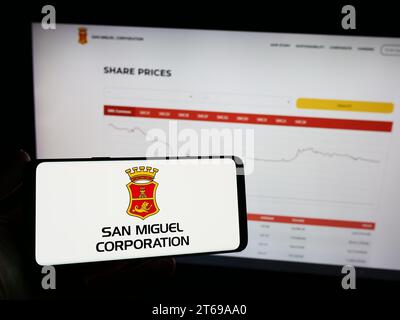 Person, die ein Mobiltelefon mit dem Logo der philippinischen Firma San Miguel Corporation (SMC) vor der Business-Webseite hält. Schwerpunkt auf dem Display des Telefons. Stockfoto