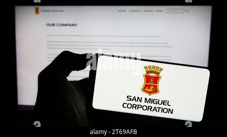 Person mit Smartphone und Logo der philippinischen Firma San Miguel Corporation (SMC) vor der Website. Schwerpunkt auf dem Display des Telefons. Stockfoto