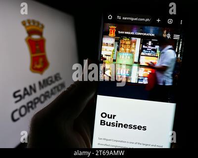 Person, die ein Mobiltelefon hält, mit Webseite der philippinischen Firma San Miguel Corporation (SMC) vor dem Logo. Konzentrieren Sie sich auf die Mitte des Telefondisplays. Stockfoto