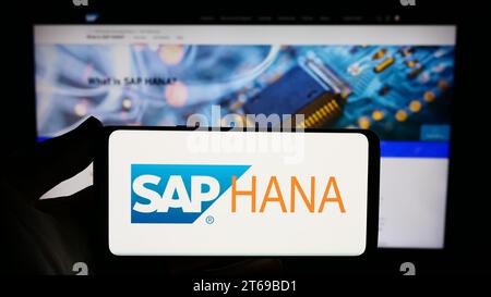 Person, die ein Smartphone mit dem Logo der Datenbankverwaltungssoftware SAP HANA vor der Website hält. Schwerpunkt auf dem Display des Telefons. Stockfoto