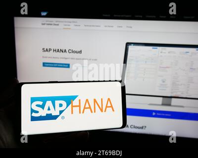 Person, die ein Mobiltelefon mit dem Logo der Datenbankverwaltungssoftware SAP HANA vor der Unternehmenswebseite hält. Schwerpunkt auf dem Display des Telefons. Stockfoto