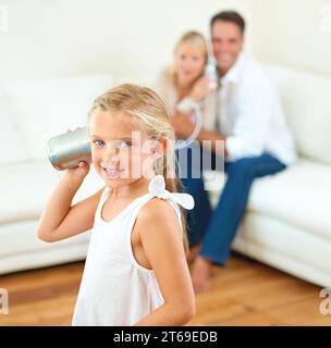Du hast meine Nummer. Ein kleines Mädchen, das durch eine Dose zuhört, verbindet sich mit ihren Eltern im Hintergrund. Stockfoto