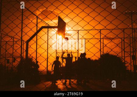 Die Silhouette von Männern, die am späten Abend draußen auf einem Platz Basketball spielen Stockfoto